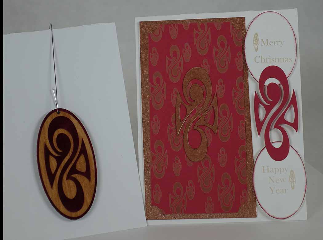 This is a picture of the 2025 Xmas ornament and card. The ornament is laser-engraved on walnut stained plywood roughly 1/16” with red foil. The card has a white background with copper & red accents.
