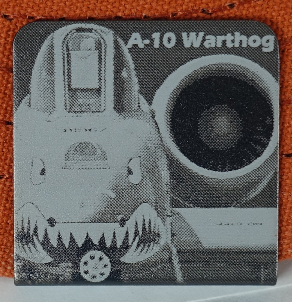 A square Approx.1.25" aluminum clip, you can accessorize your wardrobe with.  featuring a black and white pencil drawn composition  of an A-10 Warthog fighter jet, with the text 'A-10 Warthog' the image and text has been lasered onto the aluminum clip.