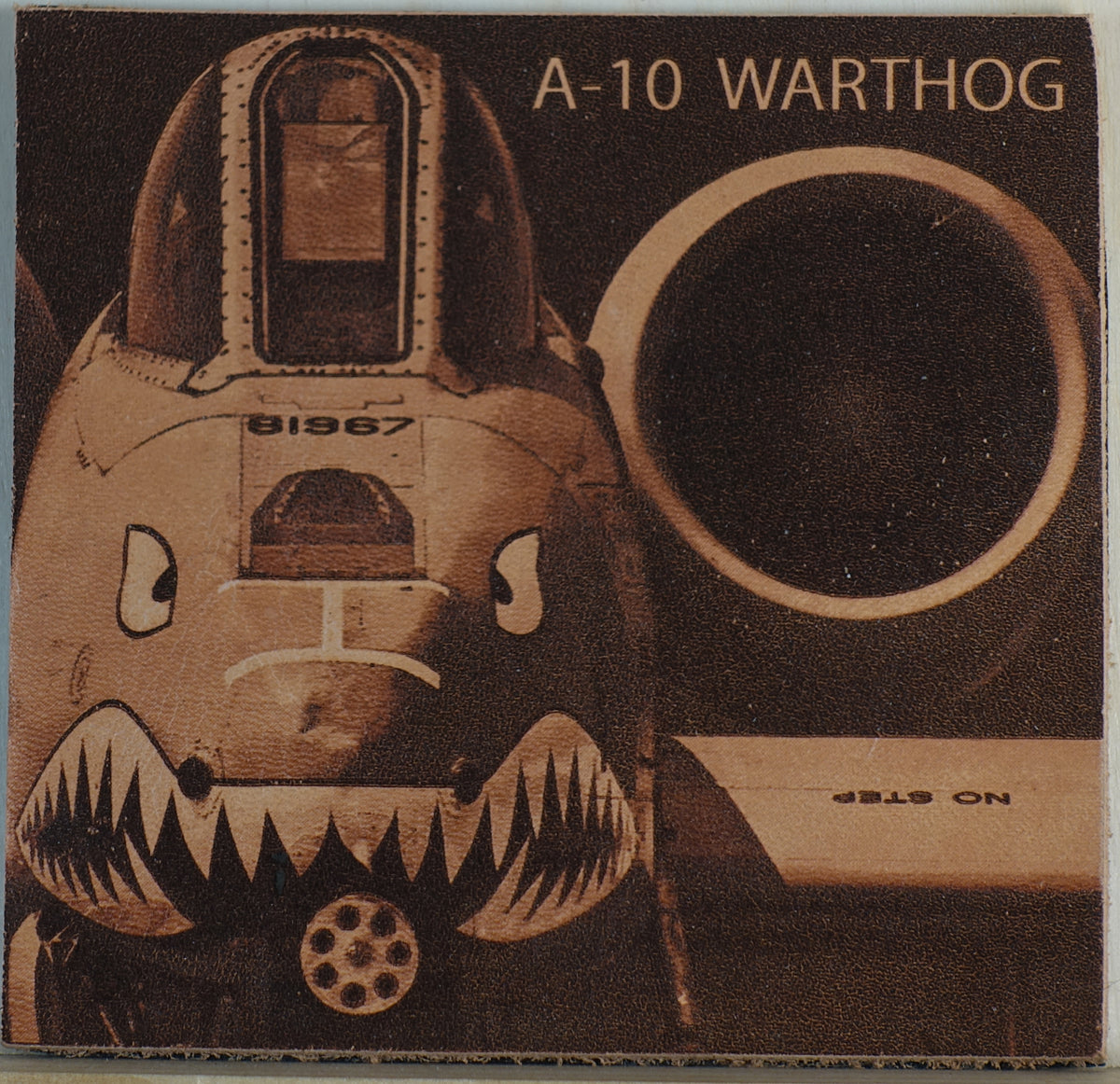 A 4"x4" patch with a composition from Michael Dean Barr of an A-10 Warthog lasered onto genuine leather featuring a stylized aircraft face with shark teeth, a large circular dark opening, and the text 'A-10 WARTHOG' at the top.