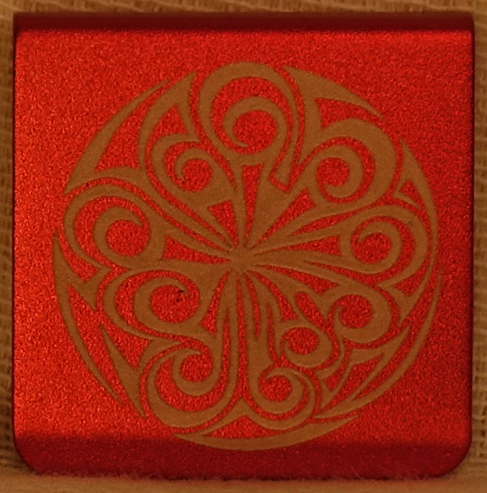 A 1.25" aluminum hat clip featuring a large circular tribal-style geometric doodle design.  The clip has round corners. 